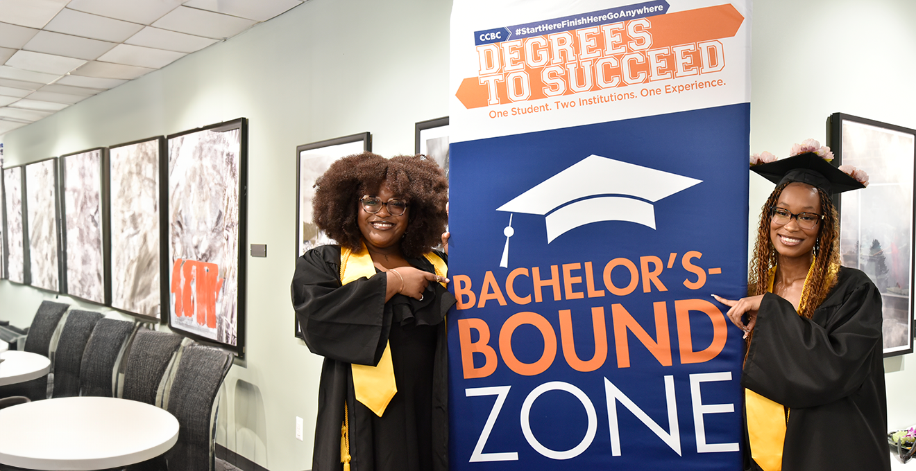 two graduates standing in front of a degrees to succeed sign