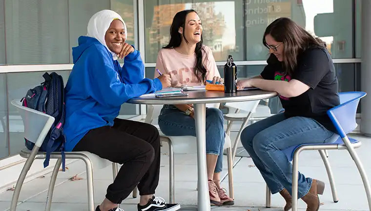 Three ccbc students studying outside on a nice day, laughing.