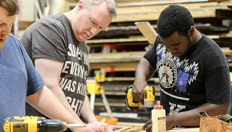 Two students in construction class using a drill