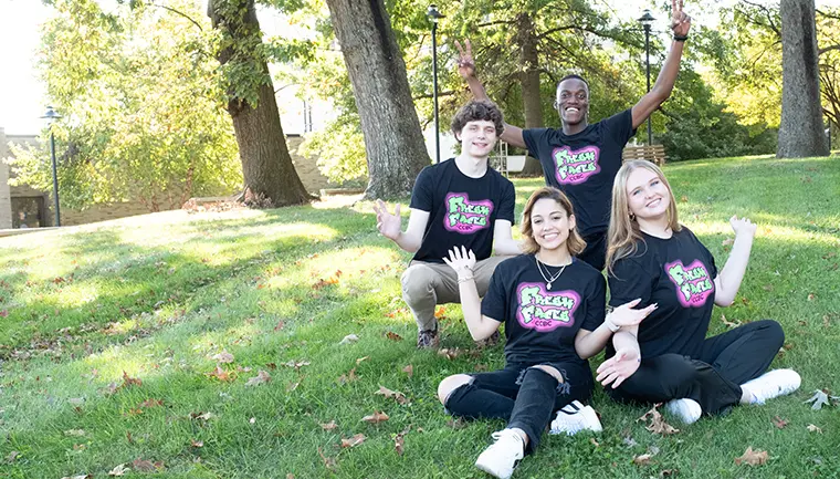 Four Fresh Faces sitting in a grassy area with their hands in the air. 