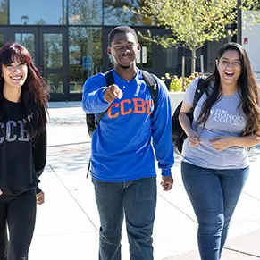 Carter stands between two students pointing forward as they walk along campus on a sunny day.