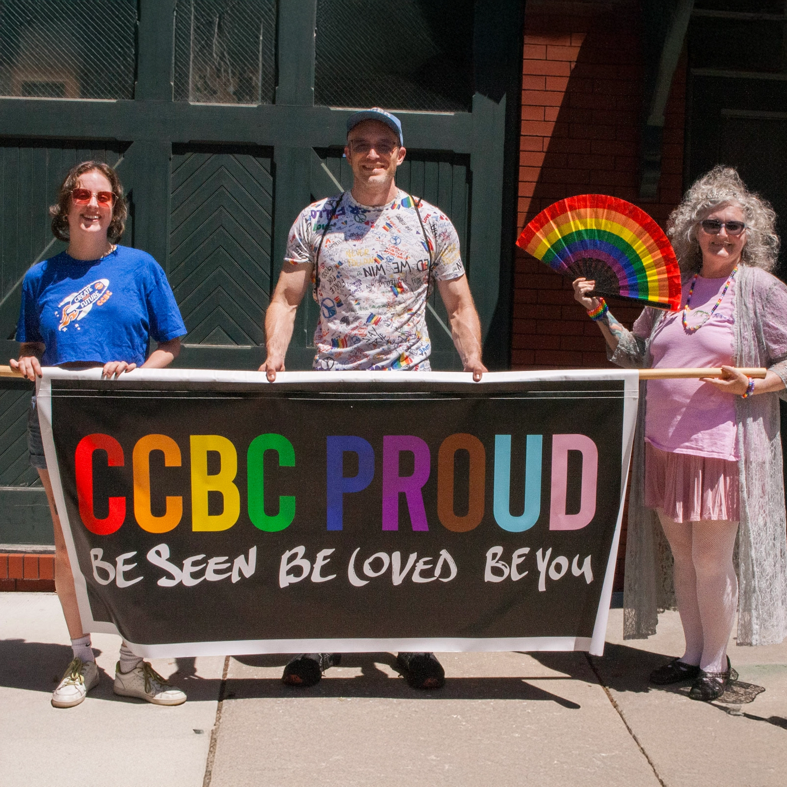 Three CCBC faculty and staff members holding a banner that reads, "Be Seen. Be Loved. Be You."
