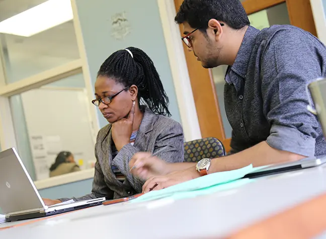 Student sits with a counselor in front of a laptop.