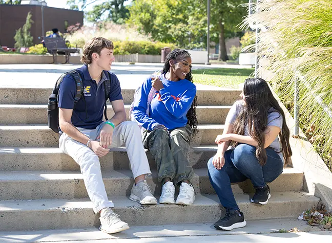 Three students sitting outside on a staircase on a sunny day.
