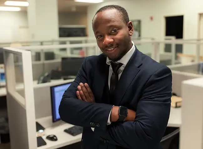 Man wearing a suit stands in front of cubicles