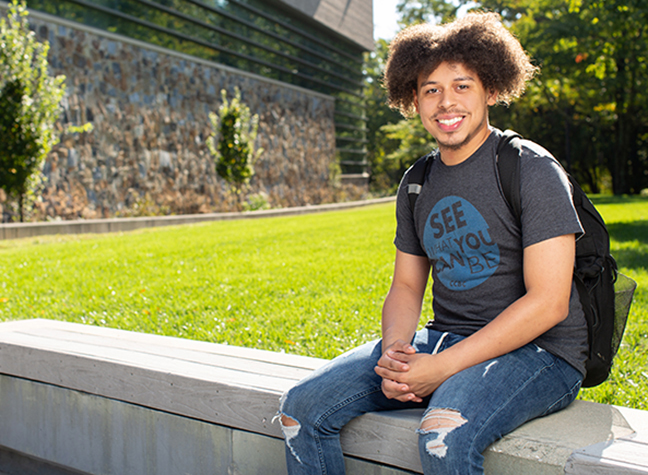 CCBC student sits in front of building on a bright and sunny day.