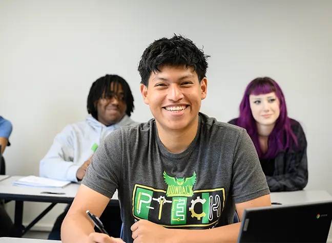 Student smiling in classroom taking notes
