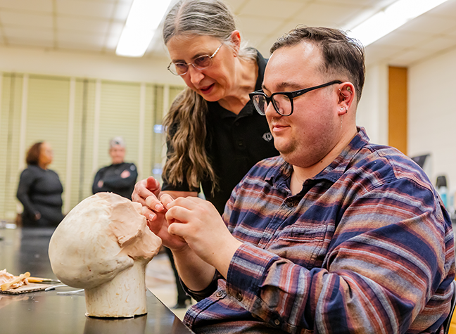 Mortuary science faculty assists a student who is sculpting a clay head
