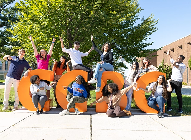Four students sitting in colorful lawn chairs on a sunny day.