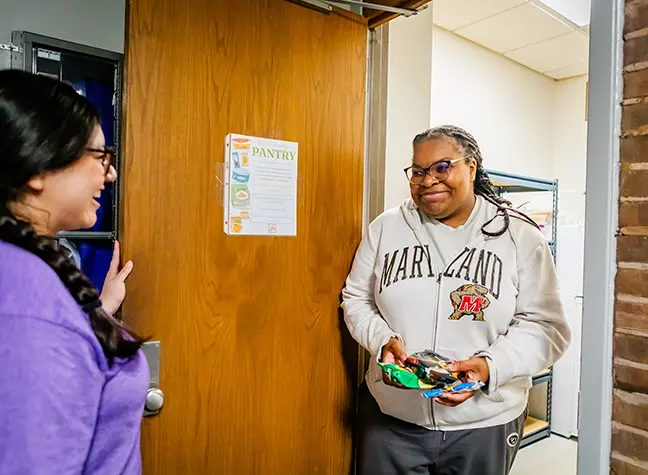 An Office of Student Engagement staff member exits the student pantry holding a handful of snacks.